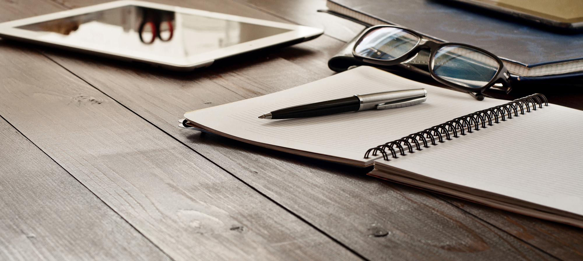 wooden desk with tablet, pen, notepaper and spectacles